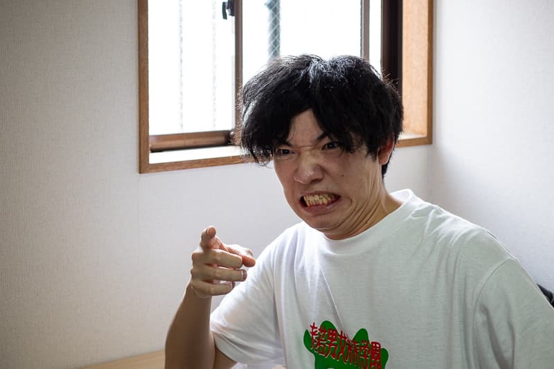 自宅にてインタヴューに答える森悟。怒った表情で人差し指を突き出している。